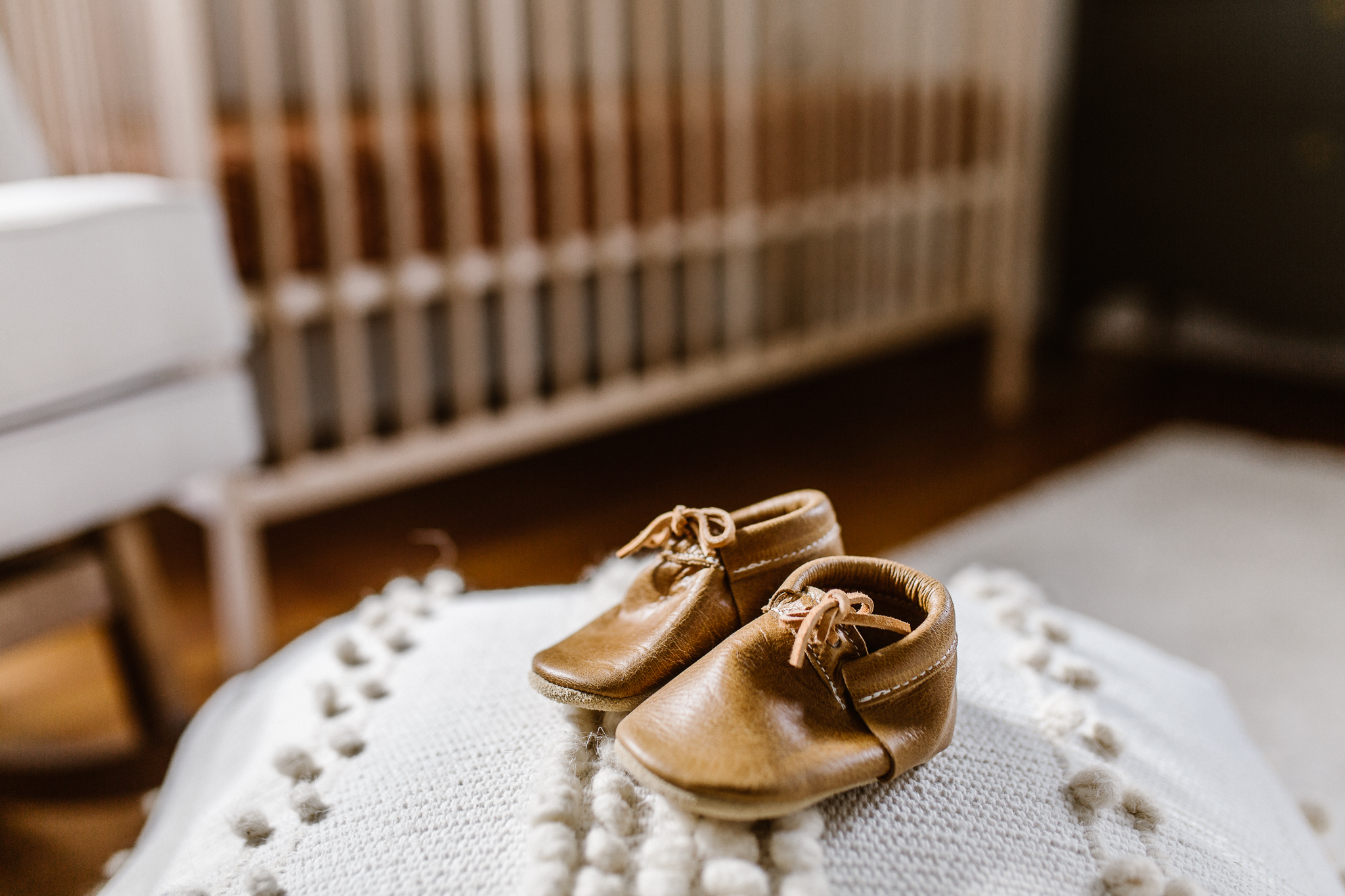 Leather baby shoes on top of a pouf in a modern nursery.